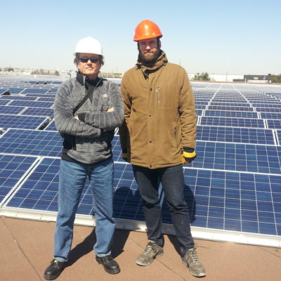 Two people standing in front of a roof of solar panels