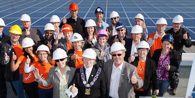 A group of people holding up their thumbs in front of solar panels